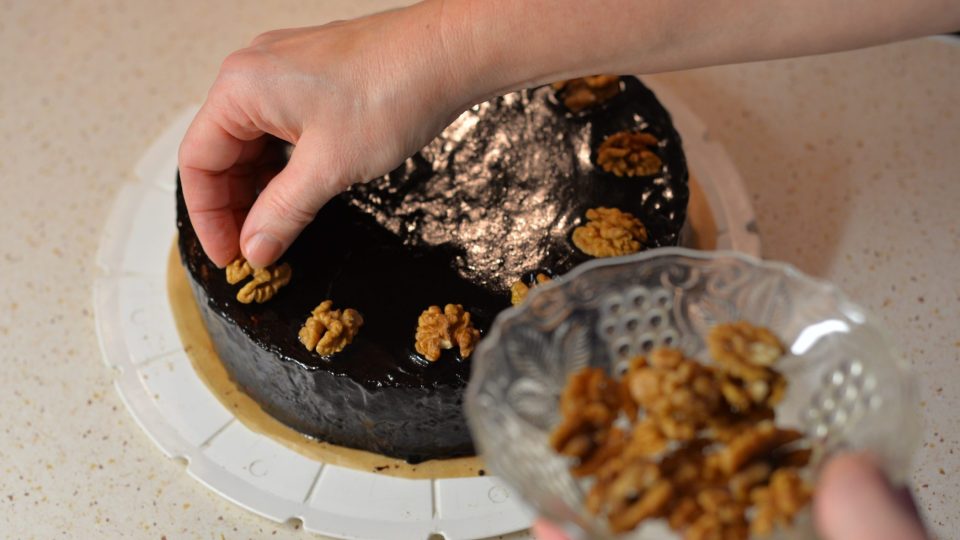 Polevou nejprve potřeme strany dortu a potom vršek. Před zatuhnutím dozdobíme půlkami ořechů | foto: Martin Čuřík Polevou nejprve potřeme strany dortu a potom vršek. Před zatuhnutím dozdobíme půlkami ořechů